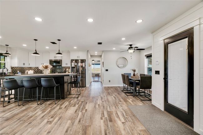 Kitchen featuring decorative backsplash, a breakfast bar, appliances with stainless steel finishes, white cabinetry, and light wood-style floors | Image 8