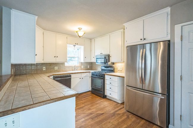 Kitchen featuring appliances with stainless steel finishes, light wood-style floors, backsplash, white cabinetry, and a peninsula | Image 6