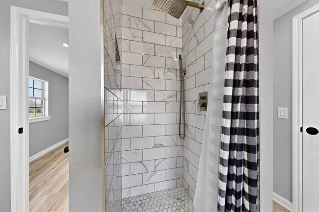 Full bath with a tile shower, baseboards, crown molding, and vinyl floors. | Image 28