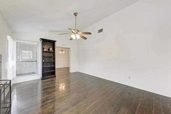 Unfurnished living room featuring dark wood finished floors, visible vents, ceiling fan with notable chandelier, and lofted ceiling | Image 9