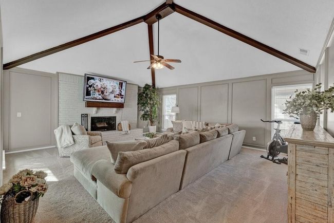Living area featuring beamed ceiling, visible vents, light colored carpet, and a decorative wall | Image 7