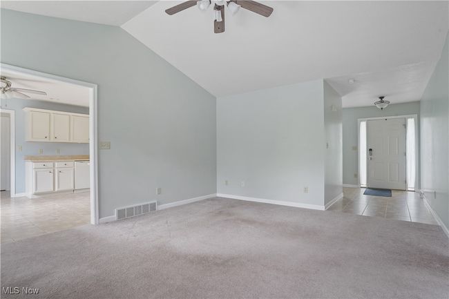 Unfurnished living room with ceiling fan, light colored carpet, vaulted ceiling, light tile patterned floors, and baseboards | Image 15