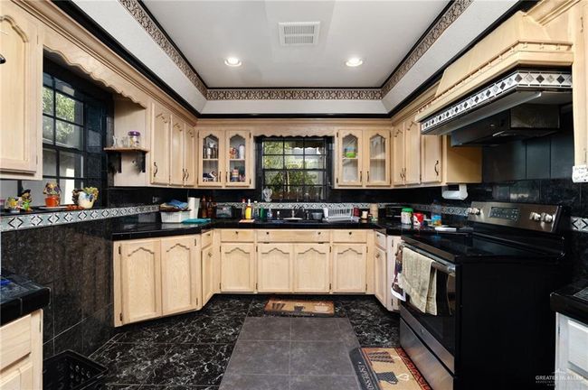 Kitchen with decorative backsplash, electric range, dark tile patterned flooring, and light brown cabinetry | Image 5
