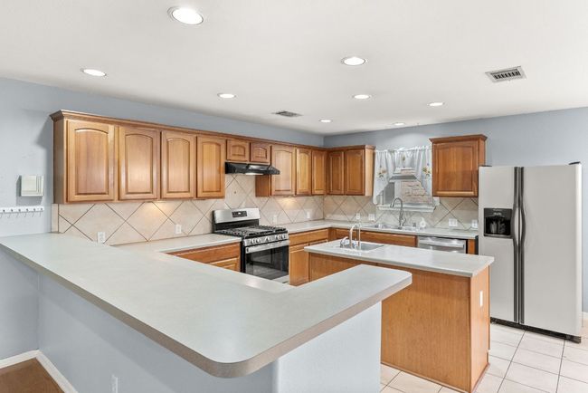 Kitchen featuring visible vents, a center island with sink, under cabinet range hood, a sink, and appliances with stainless steel finishes | Image 14