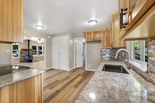Kitchen with a wood stove, tasteful backsplash, light stone countertops, light brown cabinetry, and light wood-type flooring | Image 19