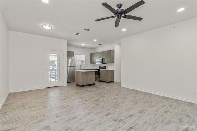 Kitchen featuring appliances with stainless steel finishes, open floor plan, a kitchen island, light countertops, and light wood-type flooring | Image 4