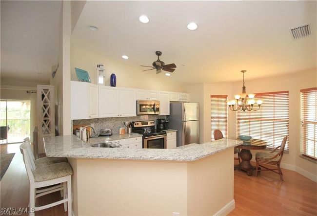 Kitchen featuring ceiling fan with notable chandelier, decorative light fixtures, stainless steel appliances, kitchen peninsula, and light wood-type flooring | Image 4