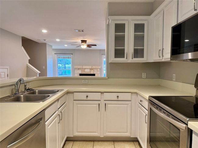 Kitchen with stainless steel appliances, ceiling fan, white cabinetry, a fireplace, and light countertops | Image 8