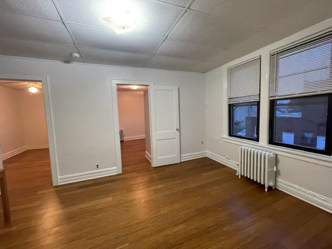 Unfurnished room featuring radiator heating unit, wood finished floors, baseboards, and a drop ceiling | Image 10