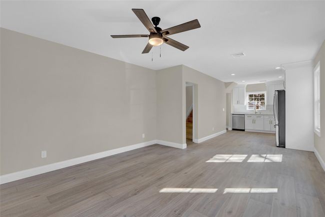 Unfurnished living room with light wood-style flooring, visible vents, a ceiling fan, baseboards, and stairway | Image 12
