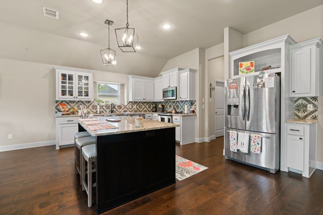 Kitchen with stainless steel appliances, open shelves, tasteful backsplash, a center island, and light stone countertops | Image 7