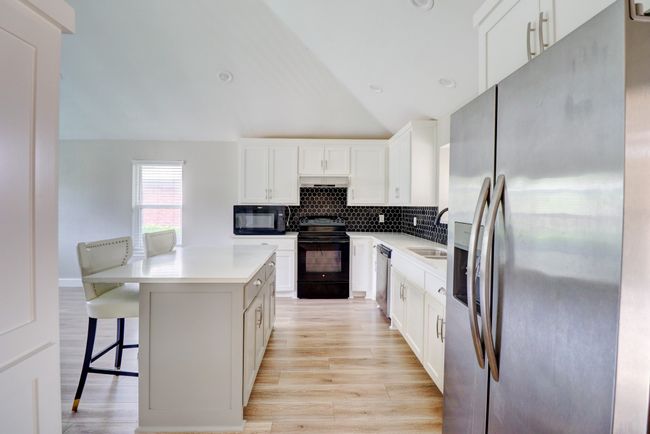 Kitchen with black appliances, light wood-style flooring, a breakfast bar area, lofted ceiling, and backsplash | Image 11