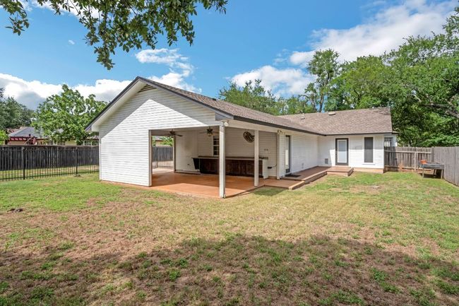 Rear view of property with a ceiling fan, a fenced backyard, patio and mature trees along fence line | Image 26