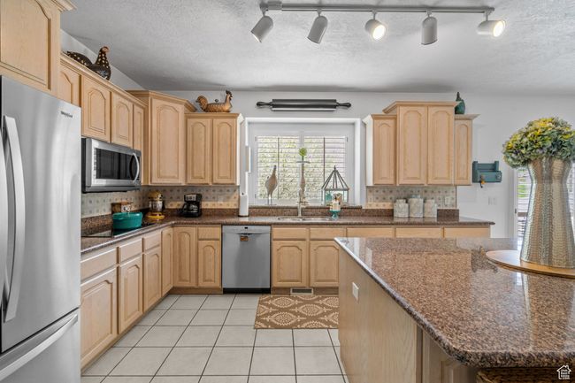 Kitchen featuring decorative backsplash, light brown cabinets, a sink, appliances with stainless steel finishes, and light tile patterned floors | Image 13
