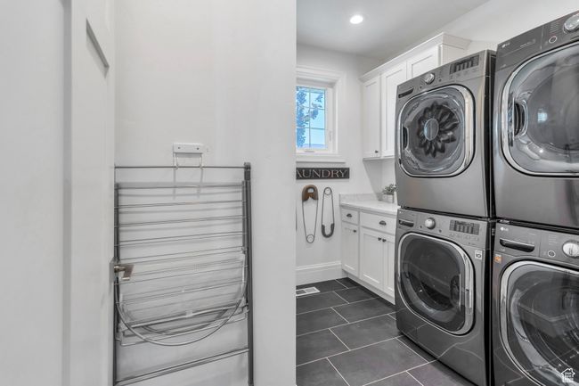 Washroom with cabinet space, independent washer and dryer, stacked washer and clothes dryer, dark tile patterned flooring, and recessed lighting | Image 27