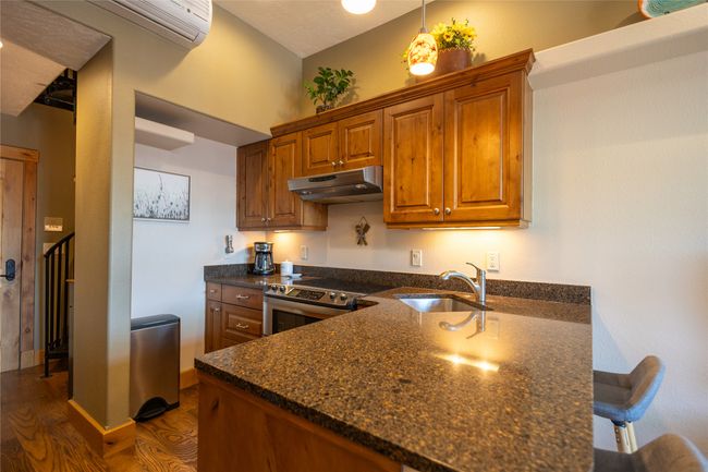 Kitchen with stainless steel range with electric stovetop, under cabinet range hood, dark wood-style flooring, brown cabinets, and a peninsula | Image 8