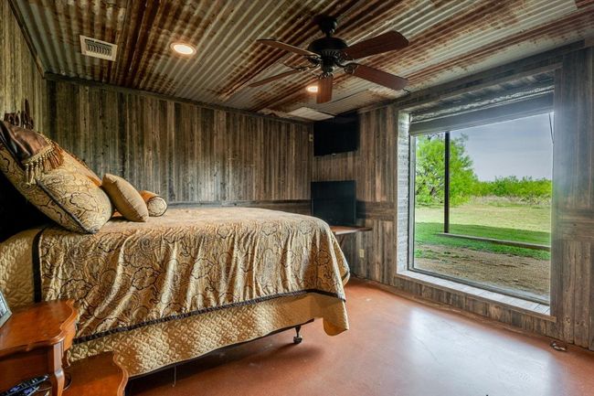 Bedroom with wooden walls, visible vents, finished concrete floors, and a ceiling fan | Image 21