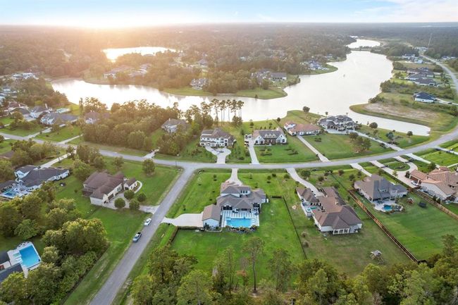 This aerial photo showcases a picturesque neighborhood with spacious homes, large yards, and a scenic lake view. The area is lush with greenery, offering a serene and upscale residential setting. | Image 7