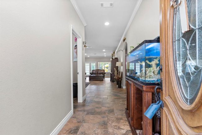 This is a spacious hallway with tiled flooring, leading into a well-lit living area. To the right, there's an ornate aquarium on a wooden stand, adding a unique decorative element to the space. | Image 13