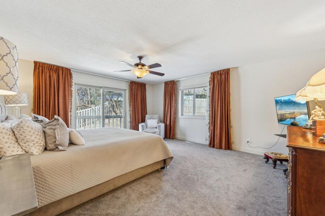 Expansive primary bedroom featuring plush carpeting, large windows with backyard views, sliding glass doors to a private patio, and space for a seating area. | Image 14