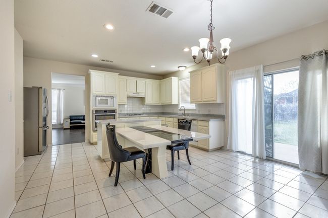 Kitchen with decorative backsplash, visible vents, a notable chandelier, stainless steel appliances, and light tile patterned floors | Image 10