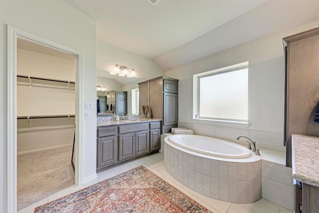 The tiled owner's bath is simply decadent, revealing separate dual granite-topped vanities and an inviting garden tub to pamper yourself. The vanity you see has its own linen/storage cabinetry. | Image 25