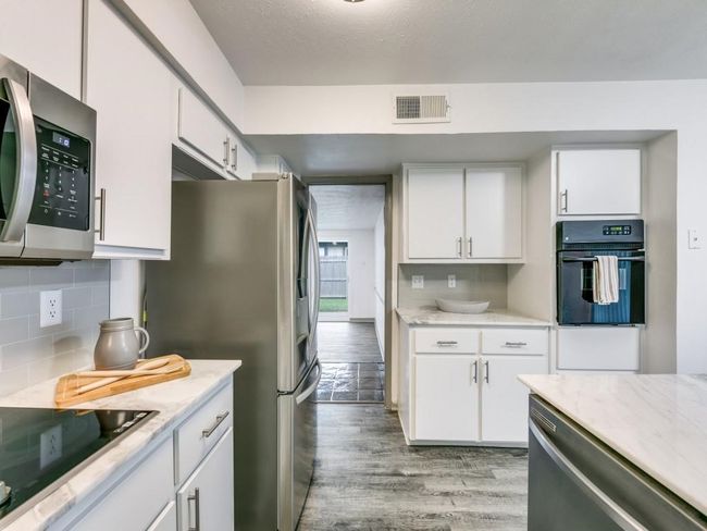 Kitchen with black appliances, light wood-style floors, white cabinets, and tasteful backsplash | Image 6