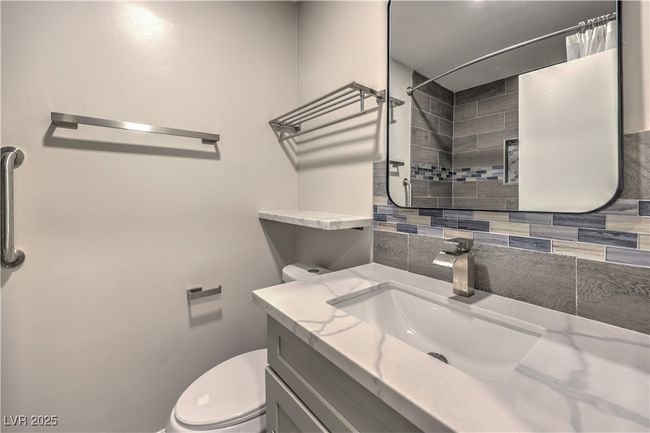 Bathroom featuring toilet, curtained shower, backsplash, and vanity | Image 31