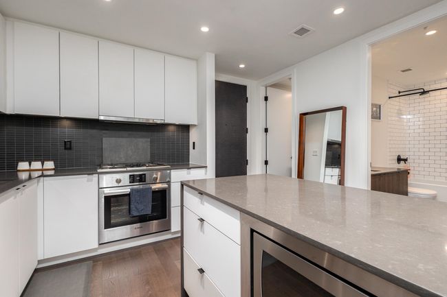Kitchen with appliances with stainless steel finishes, wine cooler, dark wood finished floors, backsplash, and white cabinetry | Image 14