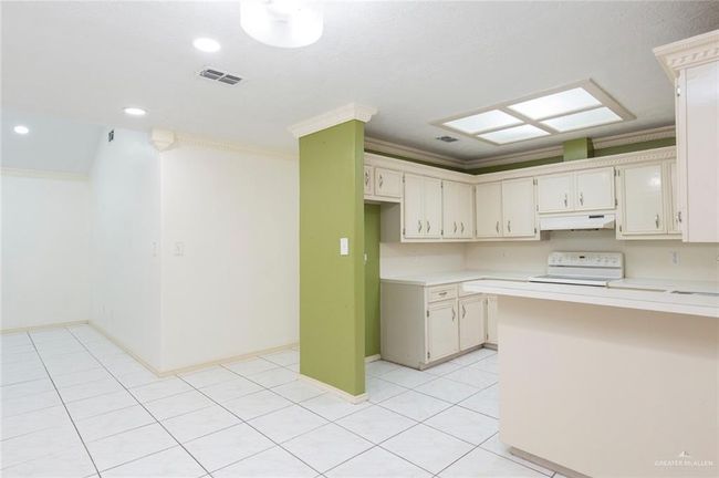 Kitchen with visible vents, under cabinet range hood, crown molding, light countertops, and range | Image 4