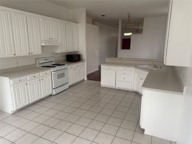 Kitchen with a sink, white gas stove, white cabinetry, under cabinet range hood, and light tile patterned floors | Image 8