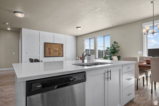 Kitchen with a textured ceiling, wood finished floors, dishwasher, a sink, and a notable chandelier | Image 13