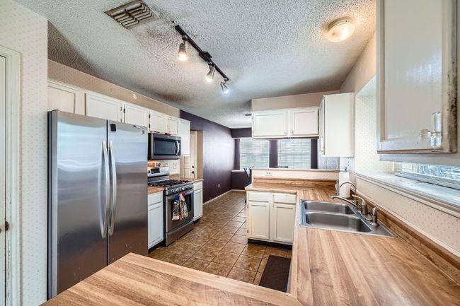 Kitchen with appliances with stainless steel finishes, wallpapered walls, white cabinetry, a textured ceiling, and a peninsula | Image 12