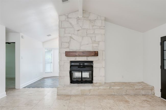 Unfurnished living room featuring a stone fireplace, lofted ceiling with beams, and tile patterned floors | Image 7