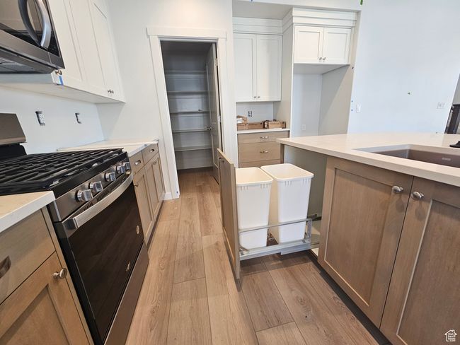 Kitchen with stainless steel appliances, light wood-type flooring, white cabinetry, and light countertops | Image 9