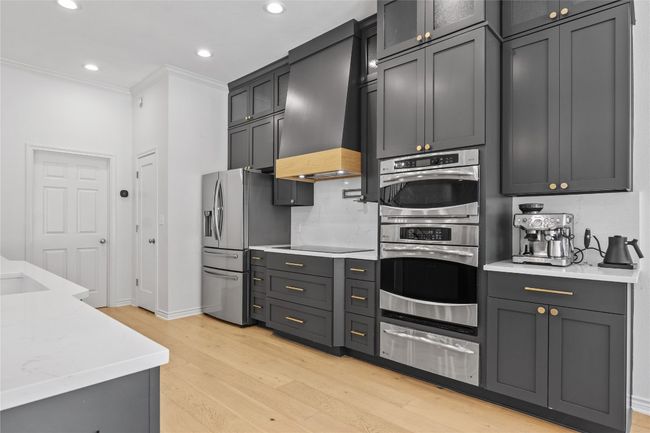 Kitchen with stainless steel appliances, a warming drawer, light wood-type flooring, crown molding, and custom range hood | Image 19