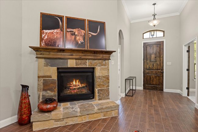 Entrance foyer with ornamental molding, wood finished floors, arched walkways, and a stone fireplace | Image 6