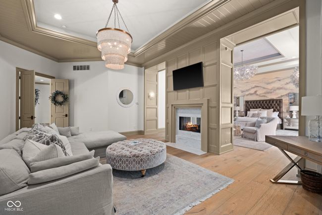 sitting area with a chandelier, light wood finished floors, ornamental molding, a premium fireplace, and a raised ceiling | Image 24
