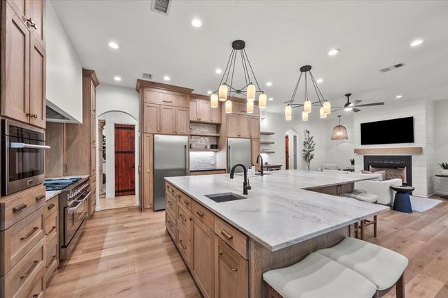 The heart of the home! This chef’s kitchen stuns with natural wood cabinetry, quartz countertops, double ovens, and a show-stopping gas range beneath a custom hood. | Image 14