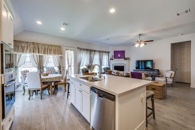 Kitchen with appliances with stainless steel finishes, a sink, a fireplace, a ceiling fan, and light wood-style floors | Image 13