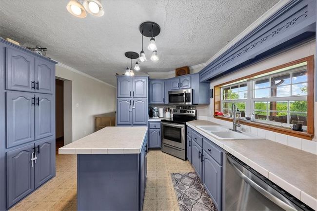 Kitchen featuring ornamental molding, stainless steel appliances, a center island, a sink, and light floors | Image 11