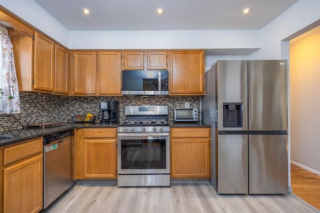 Kitchen with decorative backsplash, appliances with stainless steel finishes, light wood-style flooring, and wood cabinetry | Image 4