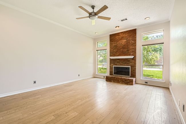 Unfurnished living room with light wood-type flooring, crown molding, a ceiling fan, a brick fireplace, and a textured ceiling | Image 10