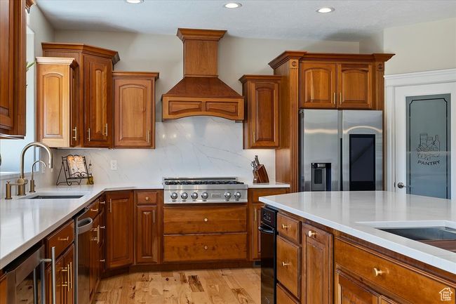 Kitchen with wine cooler, premium range hood, light countertops, a sink, and stainless steel appliances | Image 15