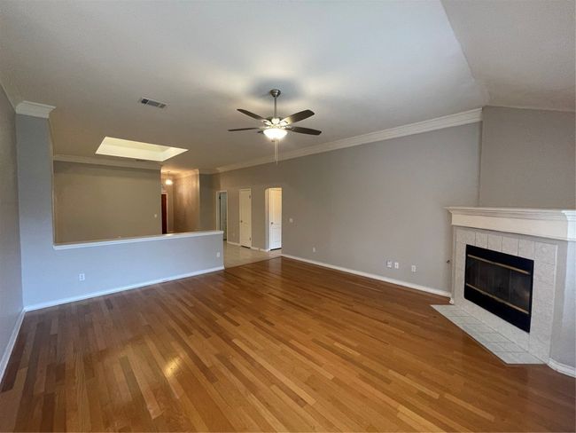 Unfurnished living room featuring wood finished floors, ceiling fan, a tiled fireplace, ornamental molding, and a skylight | Image 17