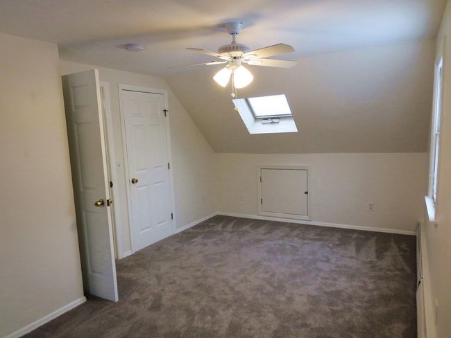 Apartment bedroom featuring vaulted ceiling with skylight, a ceiling fan, baseboards, and dark carpet | Image 11