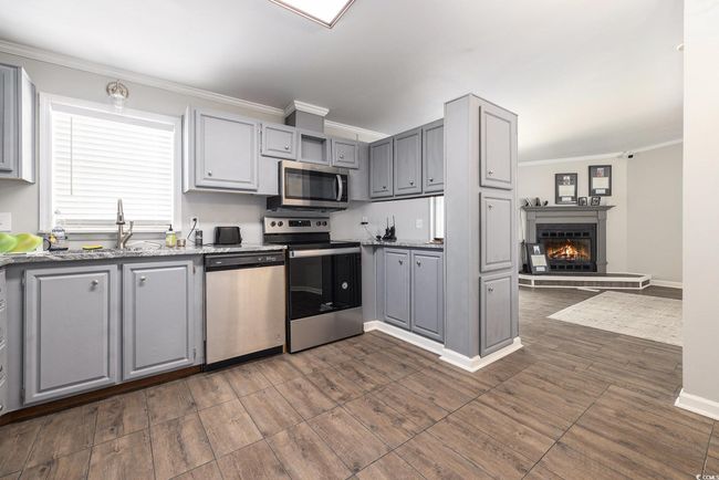 Kitchen featuring appliances with stainless steel finishes, gray cabinets, crown molding, dark wood finished floors, and a fireplace | Image 14
