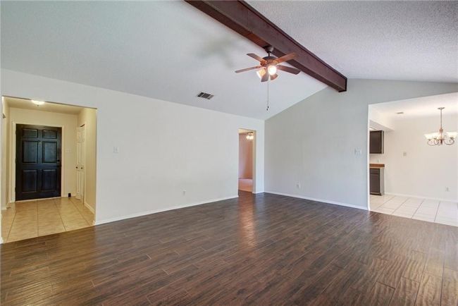 Unfurnished living room with baseboards, ceiling fan, vaulted ceiling with beams, gas fireplace. | Image 10