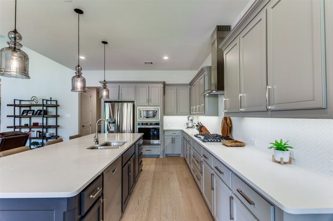 Kitchen featuring stainless steel appliances, gray cabinets, light wood-type flooring, wall chimney range hood, and decorative backsplash | Image 17