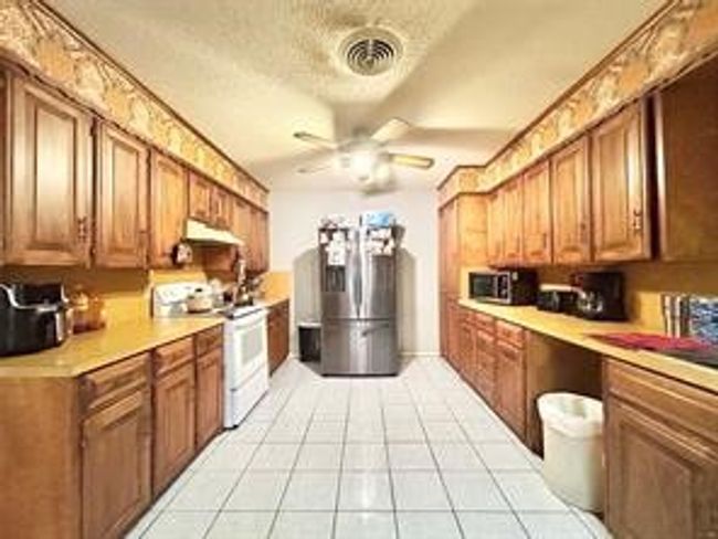 Kitchen with light tile patterned floors, visible vents, stainless steel appliances, light countertops, and under cabinet range hood | Image 7